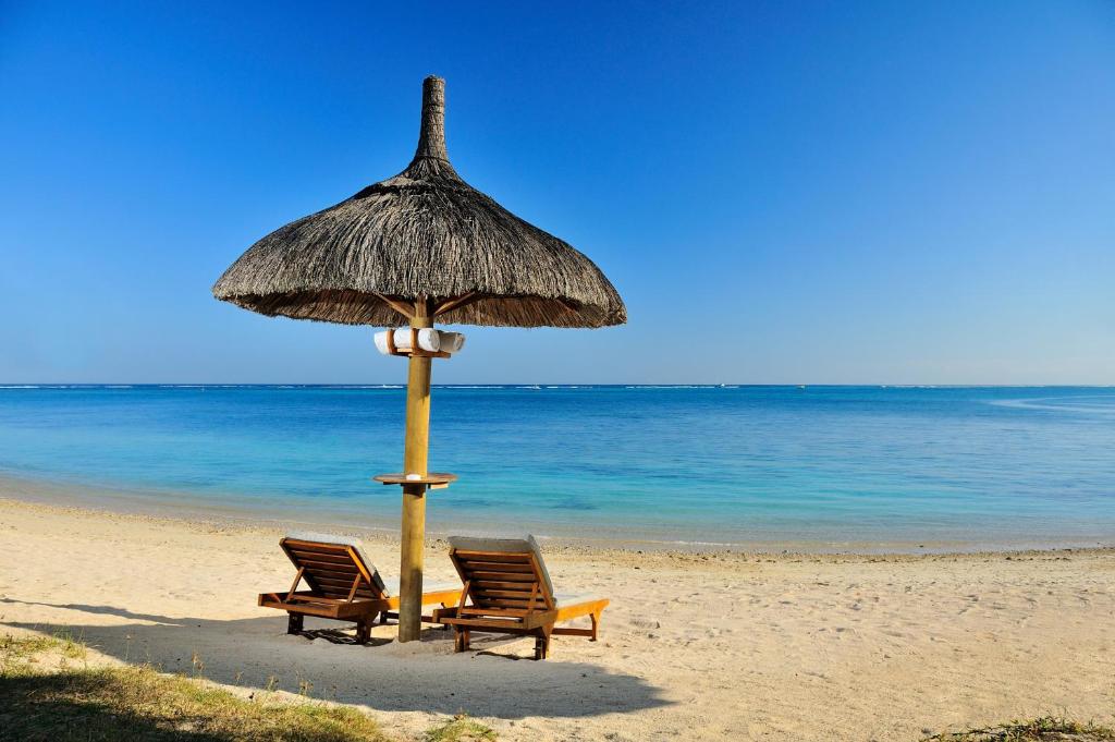 Pludmales ainava ar divām sauļošanās krēslām zem salmu jumta un skatu uz mierīgu, zilo jūru.