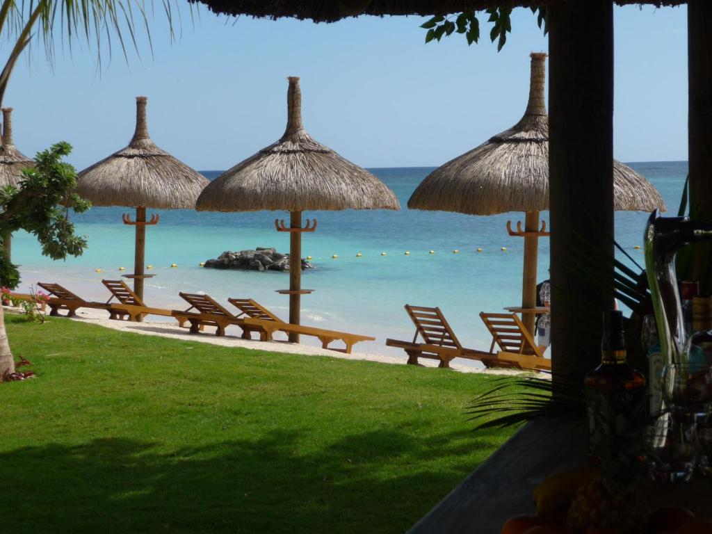 Pludmales ainava ar salmu jumtiem un sauļošanās krēsliem pie kristāldzidra ūdens. Ideāla atpūtas vieta tropiskā vidē.