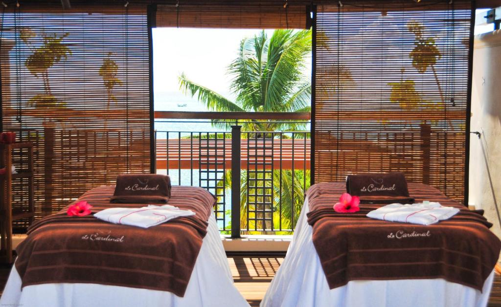 Relaksējoša masāžas telpa ar skatu uz jūru, kur divi masāžas galdi ir sagatavoti ar dvieļiem un ziediem. Daba un mierīga atmosfēra papildina atpūtas pieredzi.