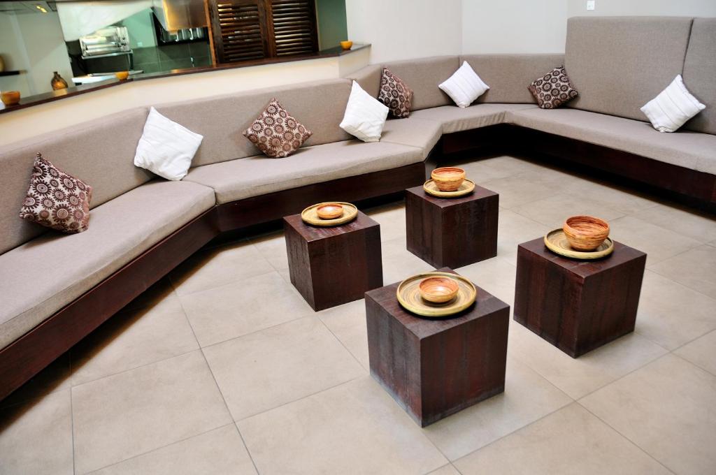 Mūsdienīgs viesistabas stūris ar pelēku dīvānu un dekoratīviem spilveniem, ap kuru izvietoti koka galdi ar traukiem. Eleganta un stilīga telpa relaksācijai.