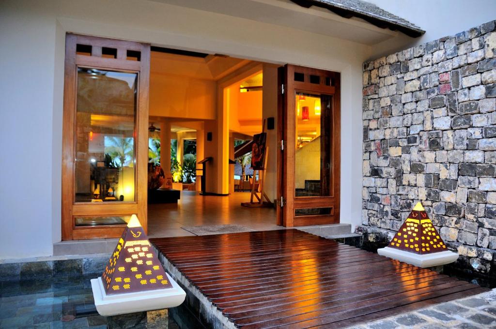 Elegants ieeja ar koka durvīm, kas ved uz gaišu un plašu interjeru, ar akmens sienu un dekoratīvām piramīdām priekšā.