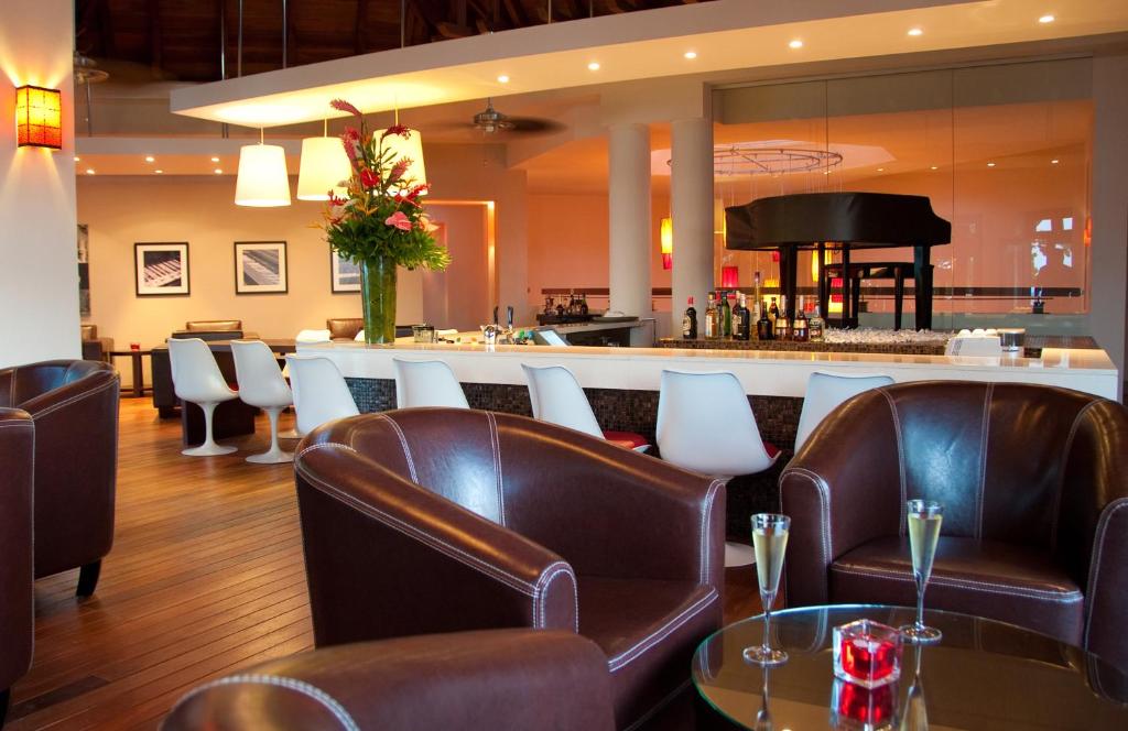 Eleganta bāra iekārtojums ar brūnām ādas krēslām un stilīgu galdu. Interjerā redzami ziedi, dzērieni un gaismas elementi, kas rada siltu atmosfēru.