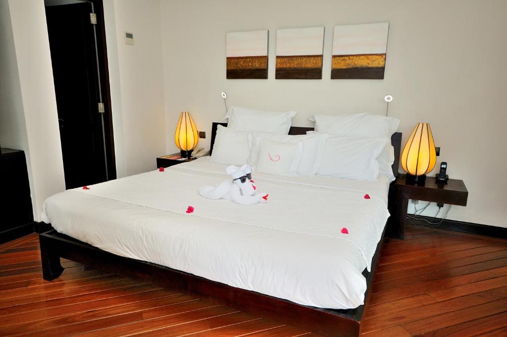 Romantiska guļamistaba ar plašu gultu, dekorēta ar rožu ziedlapiņām un baltiem spilveniem, papildināta ar stilīgām lampām un mākslas darbiem uz sienas.