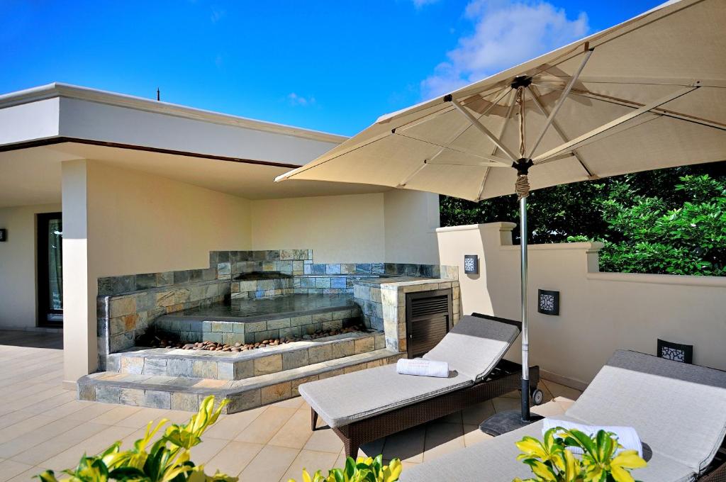 Relaksējoša terase ar akmens ūdens strūklaku, saules sēdekļiem un lielu saulessargu, apņemta ar zaļumiem. Ideāla vieta atpūtai un mierīgai atmosfērai.