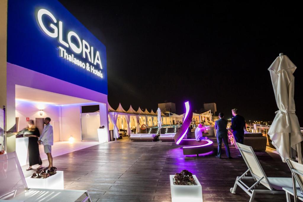 Mūsdienīga nakts ainava pie viesnīcas "Gloria Thalasso & Hotels", kurā redzami cilvēki, kas bauda atmosfēru uz terases ar mūsdienīgu apgaismojumu.