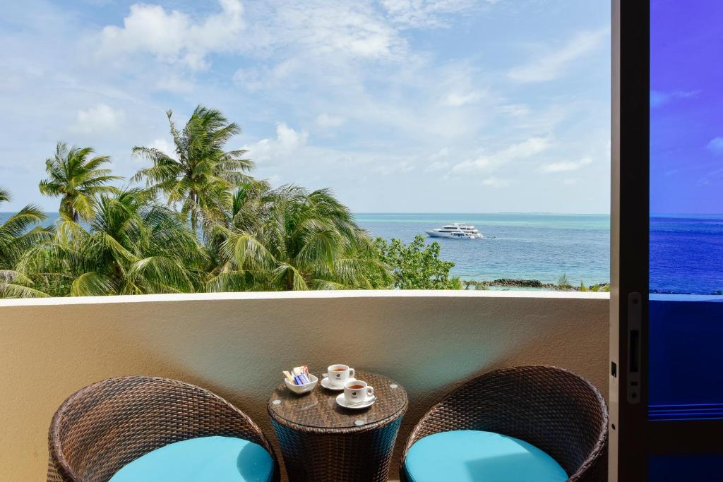 Balkons ar skatu uz jūru, palmām un laivu, uz galda divas kafijas krūzes.