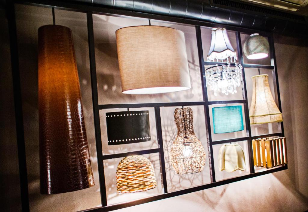 Dažādu lampu un apgaismojuma elementu kolekcija uz sienas, kas rada radošu un mājīgu atmosfēru.