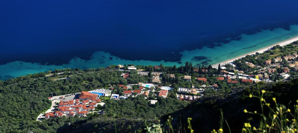 Skats uz piekrastes ciematu ar zaļām ainavām un zilo jūru. Tuvumā redzamas mājas un pludmale, kas veido skaistu harmoniju ar dabu.