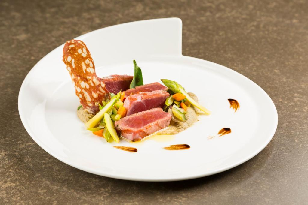 Gatavots gourmet ēdiens ar gaļas šķēlītēm, dārzeņiem un dekoratīvu cepumu uz balta šķīvja.