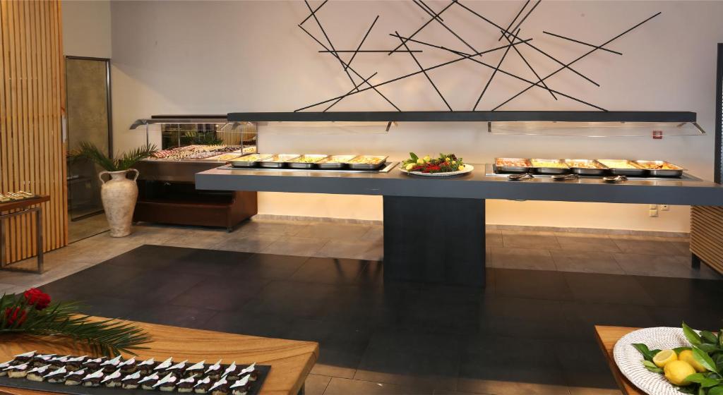 Mūsdienīga bufete ar dažādiem ēdieniem, kas novietoti uz stilīgas melnas virsmas. Interjers ir elegants un aicinošs, ar dekoratīvām detaļām un augu akcentiem.