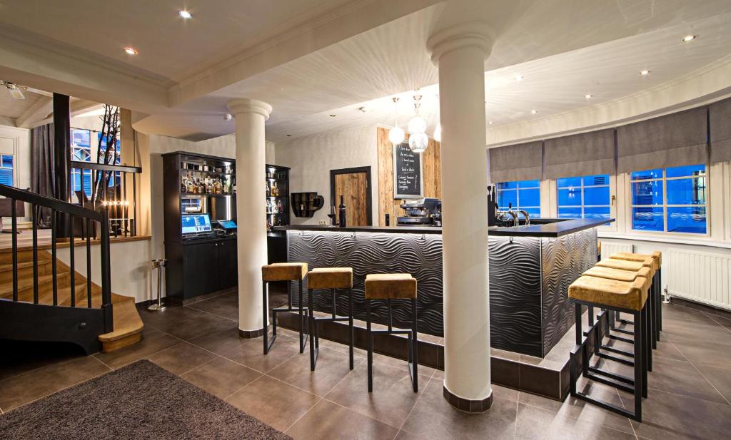 Mūsdienīgs bārs ar elegantām mēbelēm un mājīgu atmosfēru, kurā redzams bārmenis un plašs dzērienu klāsts.