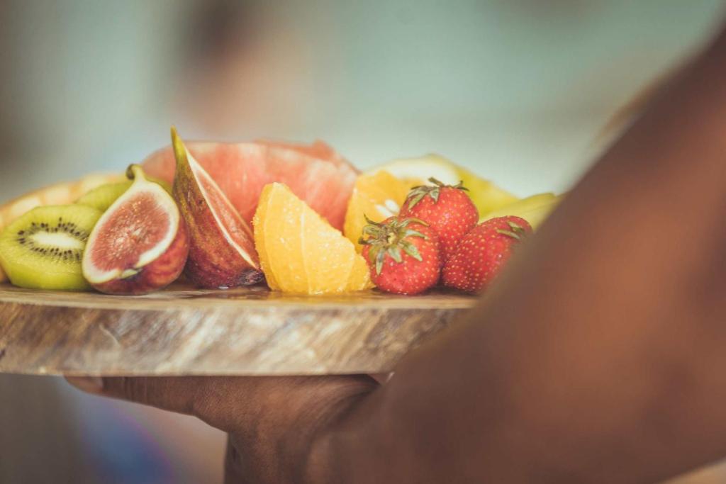 Krāsains augļu šķīvis, kas satur zemenes, vīģes, kivi, apelsīnus un greipfrūtus, tiek turēts rokā.