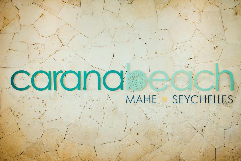 Carana Beach viesnīcas logo, kas atrodas Mahe, Seišelu salās, uz fona ar dabīgo akmens tekstūru.