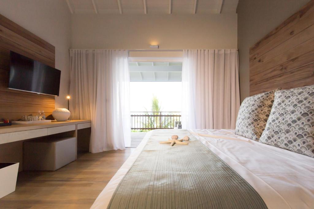 Mūsdienīga guļamistaba ar plašu logu, no kura paveras skats uz dārzu. Gultā ir dekoratīvi spilveni un jūras zvaigzne, bet blakus ir televizors un galda virsma.