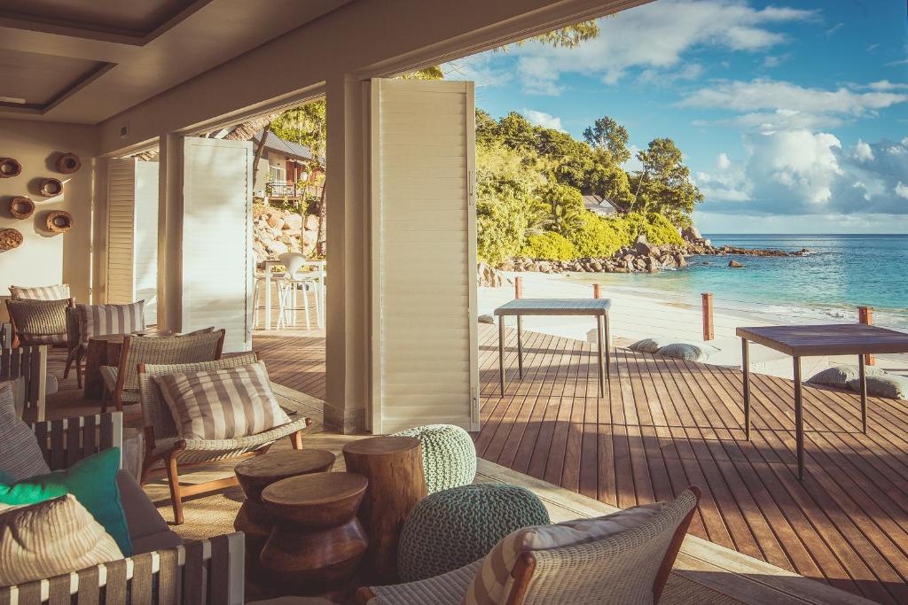 Elegants interjers ar ērtiem krēsliem un galdiem, kas piedāvā skatu uz pludmali un jūru. Dabiskais apgaismojums un zaļās ainavas rada mierīgu atmosfēru.