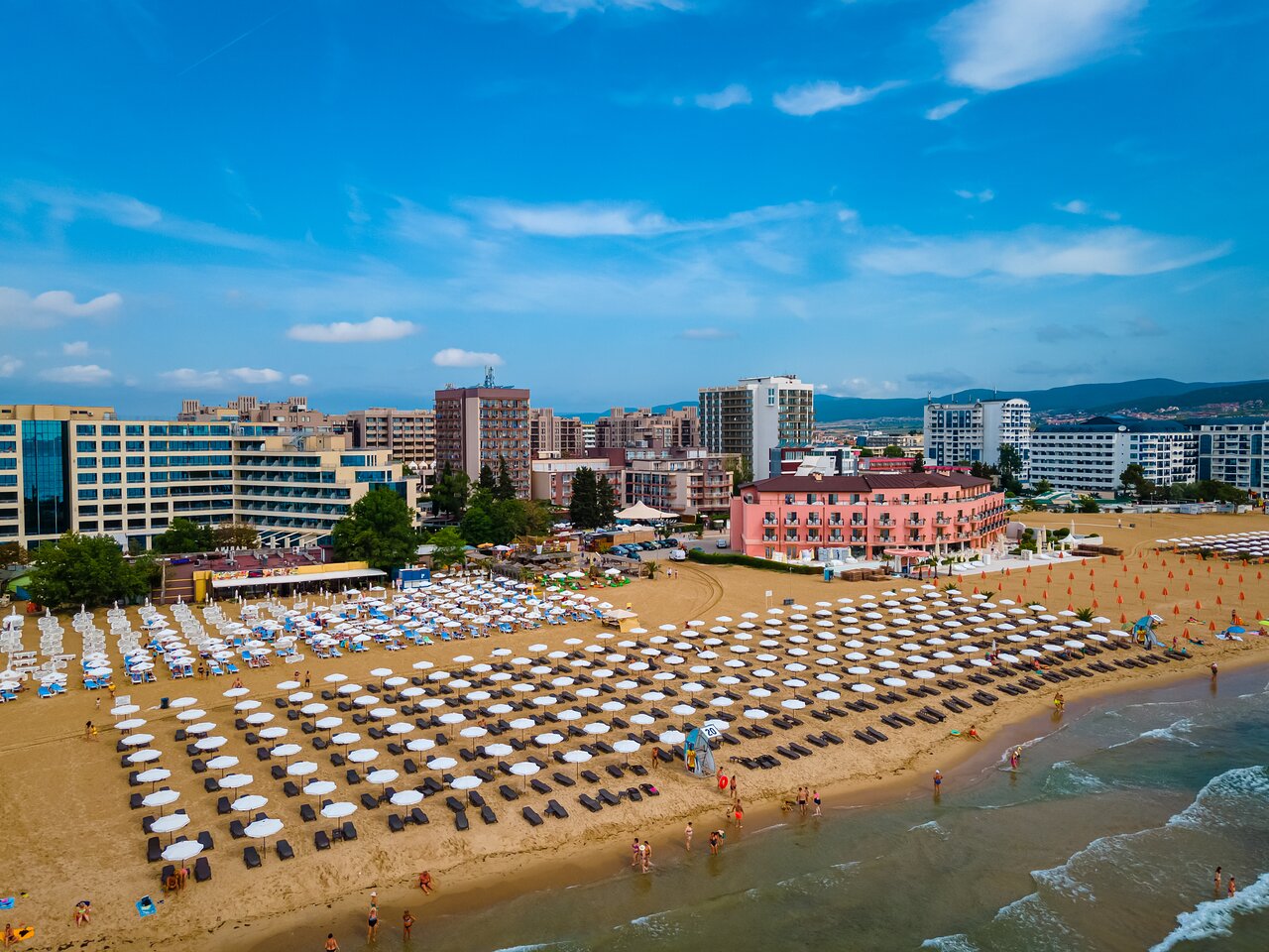Pludmales ainava ar sauļošanās krēsliem un lietussargiem, blakus viesnīcām un pilsētas ainavai. Skats uz zilo debesu un jūru. panoramic view with beach and pools