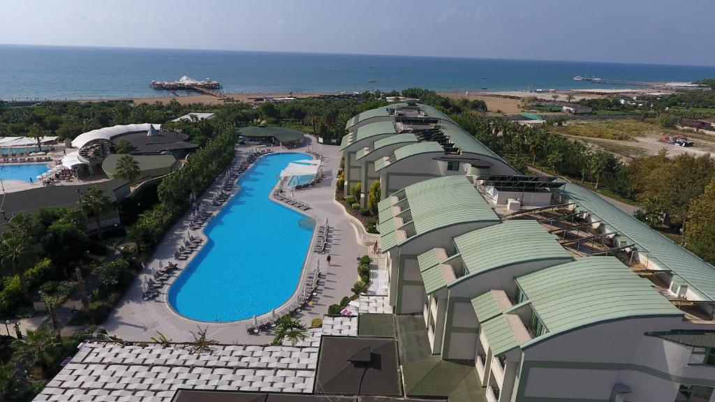 Viesnīcas komplekss ar baseinu un piekrasti, kas redzama fonā. Apkārt ir zaļi koki un tropiska veģetācija, radot relaksējošu atmosfēru.