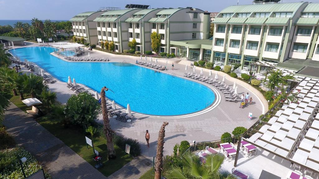 Viesnīcas komplekss ar plašu peldbaseinu un saulessargiem, apkārt esošiem zālieniem un palmām. Skats uz jūru un viesnīcas ēku.