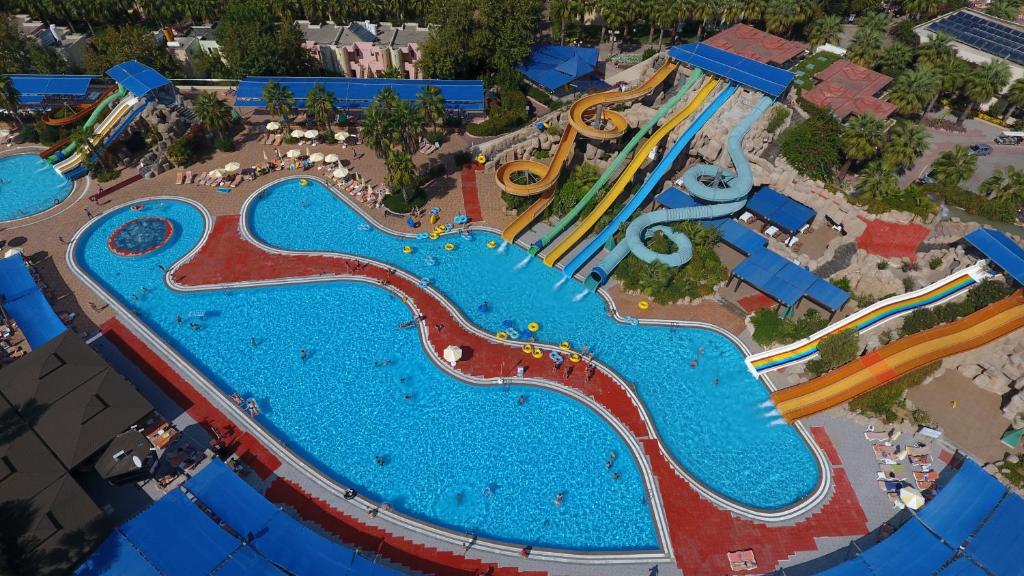Lielas ūdens atrakciju parka baseins ar dažādām slidkalniņām un atpūtas zonām, kur redzami cilvēki, kas bauda ūdens priekus.