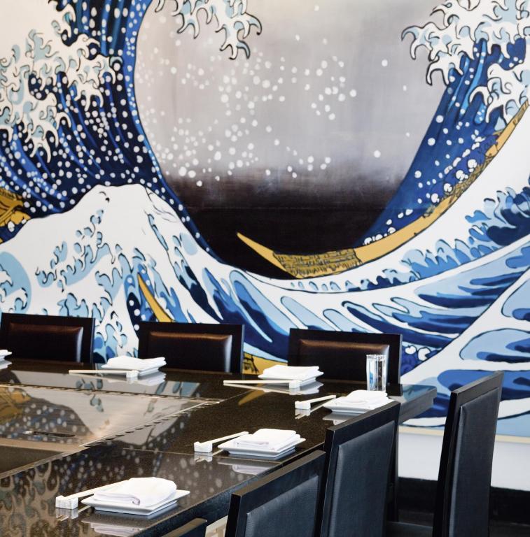 Restorāna iekārtojums ar elegantu galdu un melnu marmora virsmu, kurā redzama izsmalcināta viļņu glezna, kas piešķir telpai mājīgu un māksliniecisku atmosfēru.