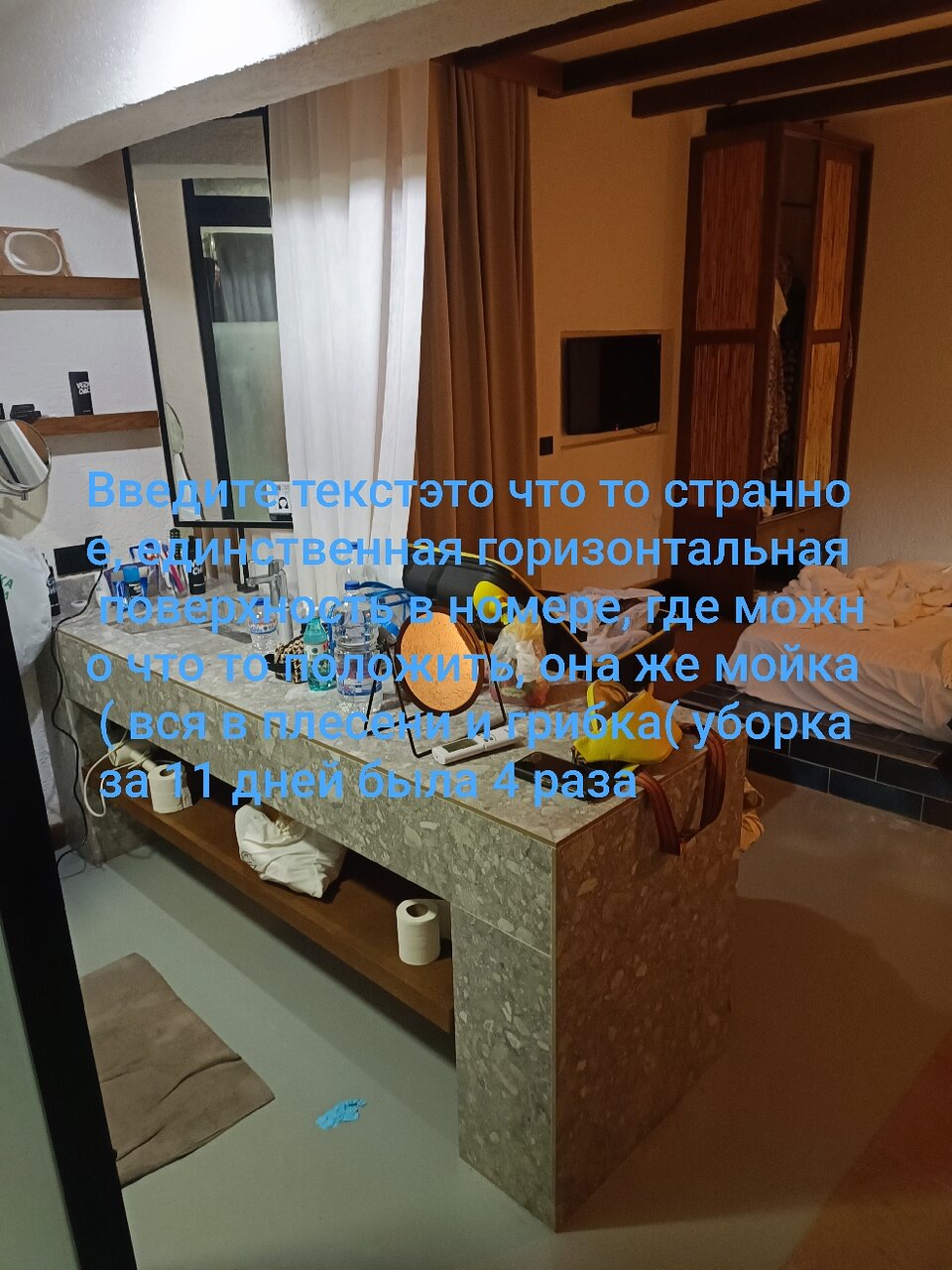 Mūsdienīgs viesnīcas numurs ar horizontālu virsmu, kas izskatās neparasti, un ar dažādiem priekšmetiem uz galda. Telpā ir arī dīvāns un televizors, bet redzamas ir arī tīrīšanas problēmas. panoramic view with beach and pools