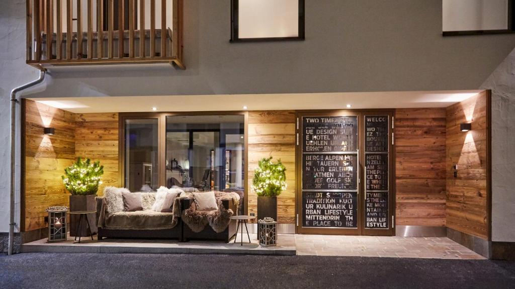 Mūsdienīgs ieejas dizains ar koka apdari, komfortablu dīvānu un dekoratīvām gaismām. Siltā atmosfērā ir redzamas arī zaļās dekoratīvās augu kompozīcijas.