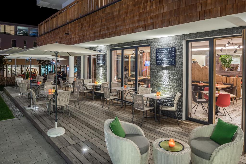 Āra kafejnīca ar mīkstiem krēsliem un galdiem, apgaismotā terasē, kurā ir redzami dzērieni un ēdienkarte. Vakarā atmosfēra ir silta un aicinoša.