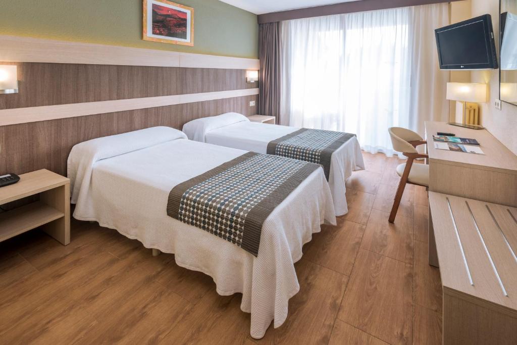 Mūsdienīga viesnīcas istaba ar divām atsevišķām gultām, koka grīdu un plašiem logiem, kas nodrošina dabiska apgaismojuma plūsmu. Istabā ir arī rakstāmgalds un televizors.