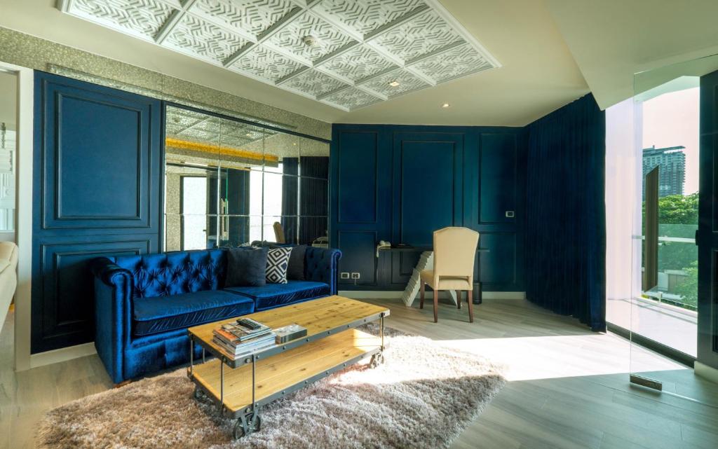 Mūsdienīga viesistaba ar tumši zilu dīvānu un koka galdiņu, kas atrodas uz mīksta paklāja. Telpa ir apgaismota ar dabīgu gaismu, un tajā ir elegants dizains ar spoguļiem un izsmalcinātām sienām.