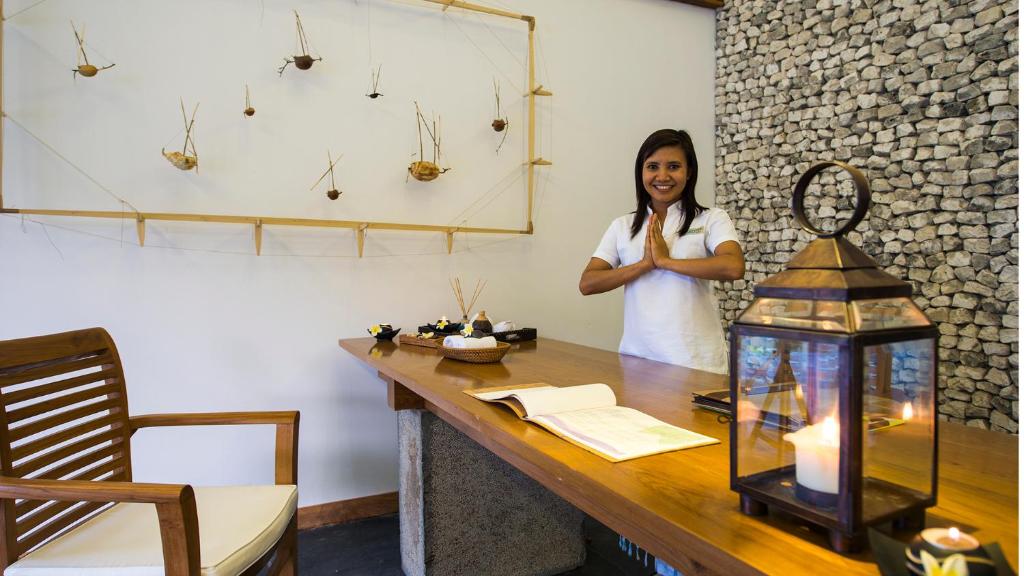 Skaista un mierīga spa recepcija ar laipnu darbinieku, kas sveicina viesus, un elegantu rotājumu no akmeņiem un piekārtiem elementiem. Gaismas avots pie galda papildina relaksējošo atmosfēru.