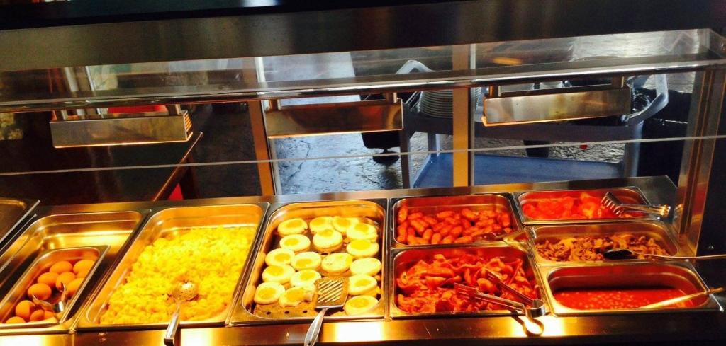 Brokastis ar dažādiem ēdieniem, tostarp olu, rīsu, desiņām un salātiem, izlikti uz bufetes galda.