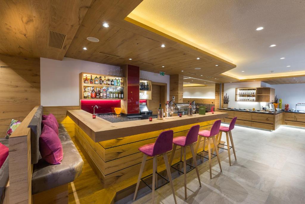 Mūsdienīgs bārs ar koka apdari un siltu apgaismojumu, kurā redzama dzērienu plauktu rinda un komfortablas sēdvietas ar spilveniem. Ideāla vieta relaksācijai un sociālai mijiedarbībai.