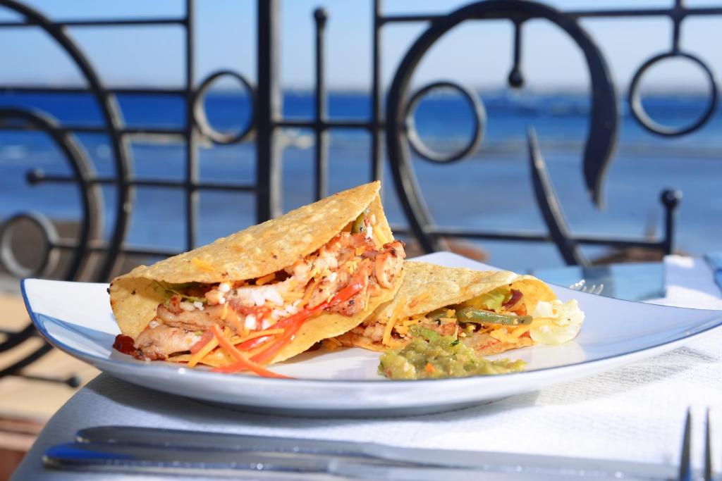 Divas garšīgas tacos, pildītas ar vistas gaļu un dārzeņiem, pasniegtas uz balta šķīvja ar jūras skatu fonā. Ideāla izvēle ikdienas ēdienreizēm vai svinībām.