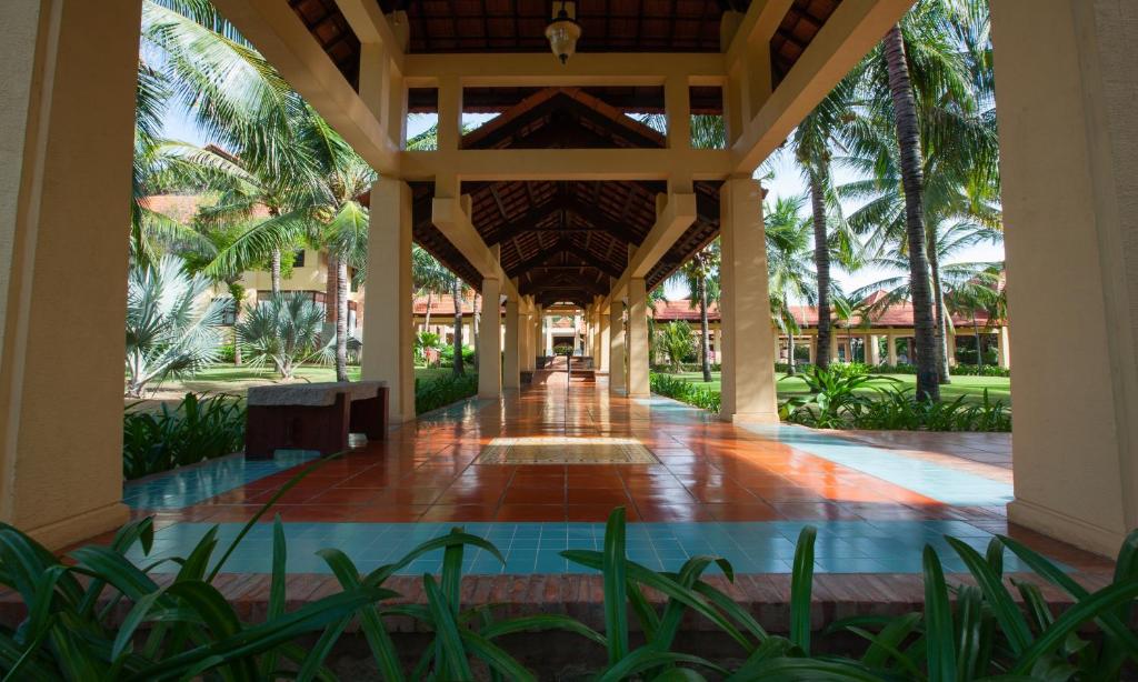 Plaša, saulaina pastaigu aleja ar palmām un augiem, kas ved uz ēku kompleksu. Uzklāts flīžu grīdas segums un izteikta arhitektūra.