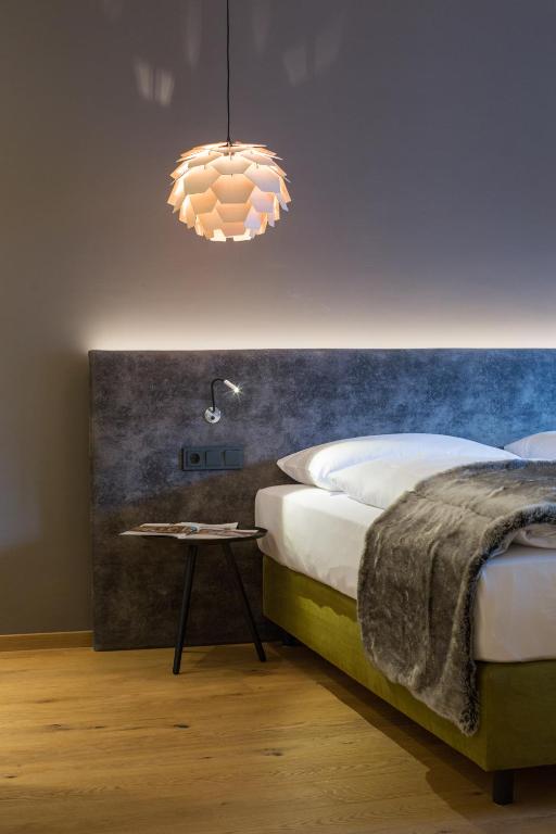 Mūsdienīgs guļamistabas interjers ar stilīgu lampu un ērtiem gultas piederumiem, radot siltu un aicinošu atmosfēru.