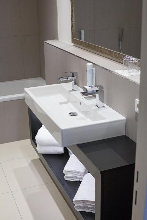 Mūsdienīgs vannasistabas izskats ar elegantu izlietni un spoguļu, kas papildina minimālisma stilu. Uz plaukta izvietoti dvieļi, radot tīru un sakārtotu vidi.