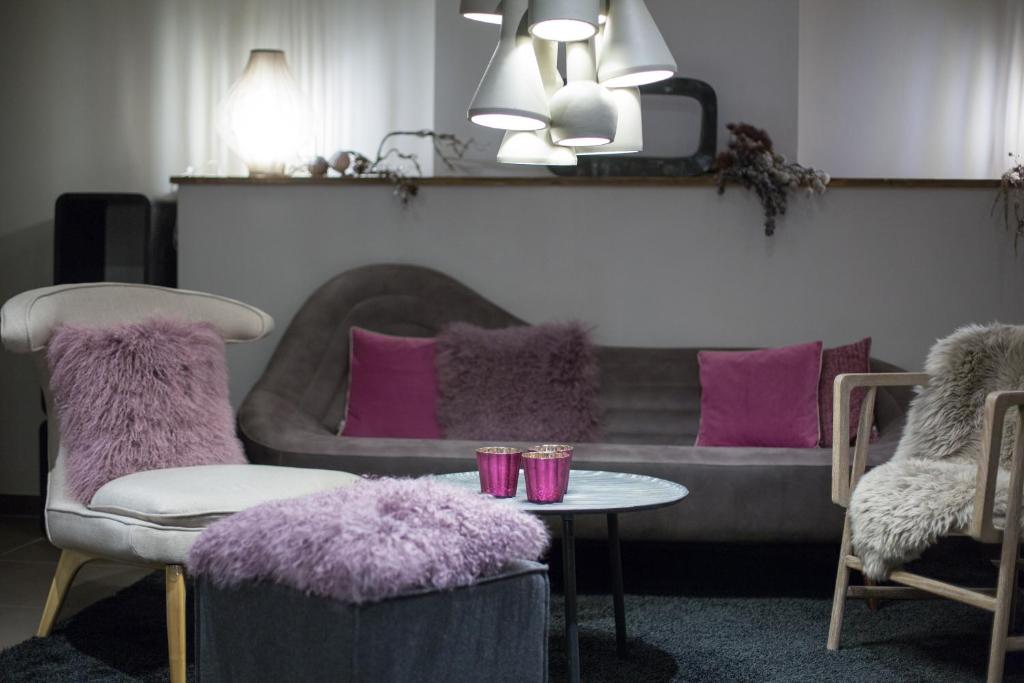 Mūsdienīgs viesistabas interjers ar pelēku dīvānu, rozā spilveniem un stilīgu apgaismojumu. Gaismas elementi un mīkstās mēbeles rada siltu un aicinošu atmosfēru.