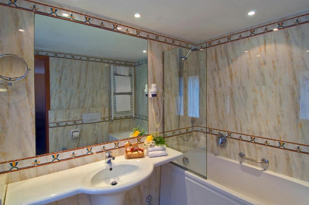 Mūsdienīgs vannas istabas interjers ar marmora apdari, vannu un izsmalcinātu spoguli. Uz izlietnes ir dekoratīva groziņa ar ziediem un dvieļiem.