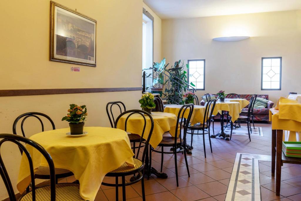 Kafejnīcas interjers ar dzeltenām galdautām un koka krēsliem, kas rada viesmīlīgu atmosfēru. Telpā ir augu kompozīcijas un glezna uz sienas, kas piešķir papildus šarmu.