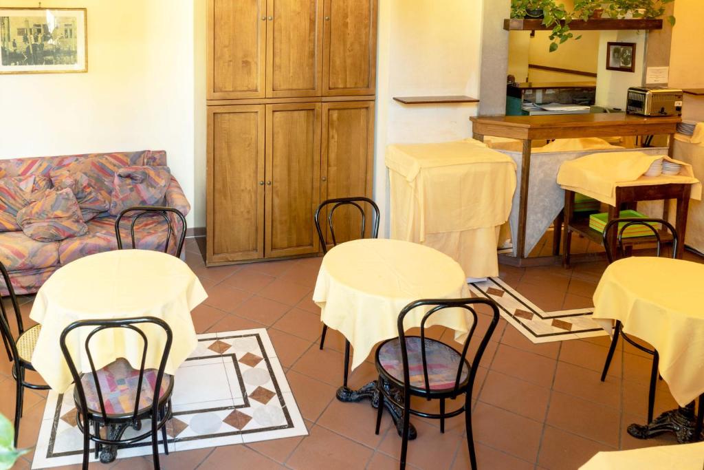 Mājīgs kafejnīcas interjers ar apaļiem galdiem un dzeltenām galdautām, brūnu koka skapjiem un krāsainu dīvānu. Gaisīga atmosfēra, ideāla vieta relaksācijai.