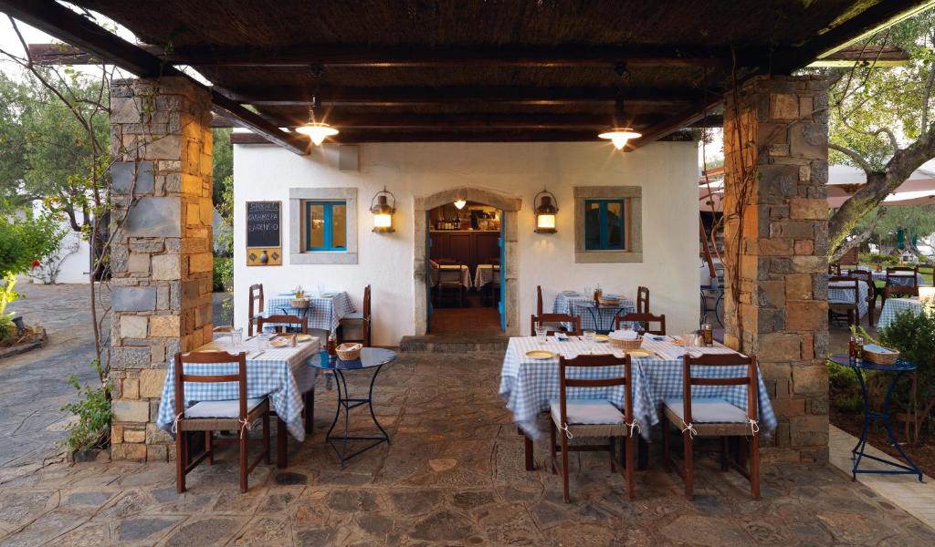 Restorāna terase ar akmens kolonnu un galdautiem ar rūtiņām, kur viesi var baudīt maltītes un relaksēties ārā. Gaismas piekari un dabiska vide rada siltu un aicinošu atmosfēru.