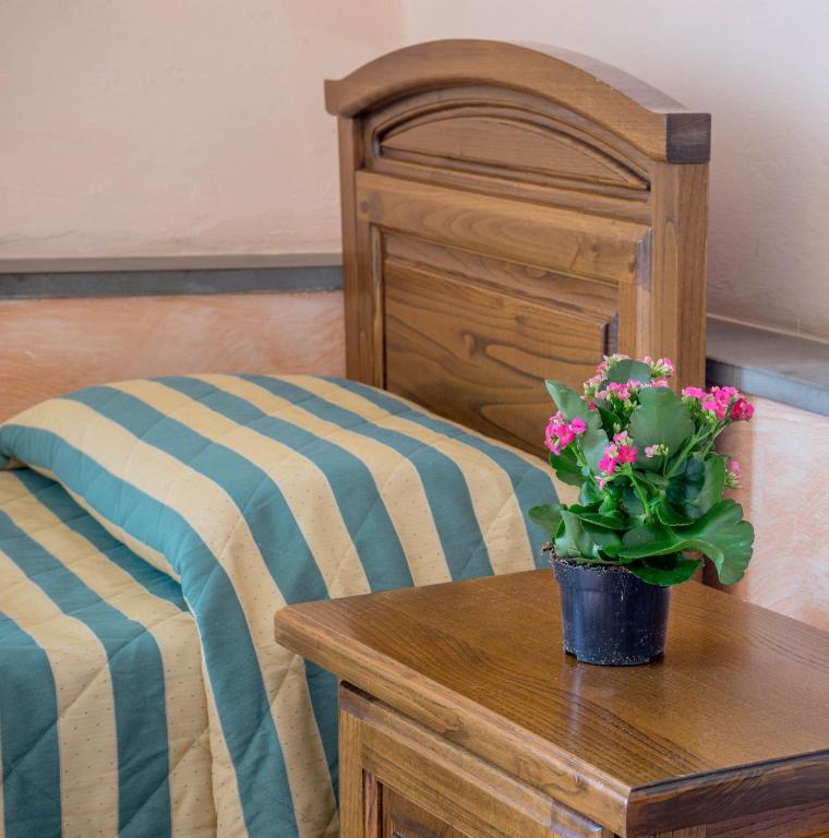 Kādas guļamistabas skats ar koka gultas galviņu un svītrainām gultas segām, blakus ir koka naktsgaldiņš ar puķu podu un ziediem.