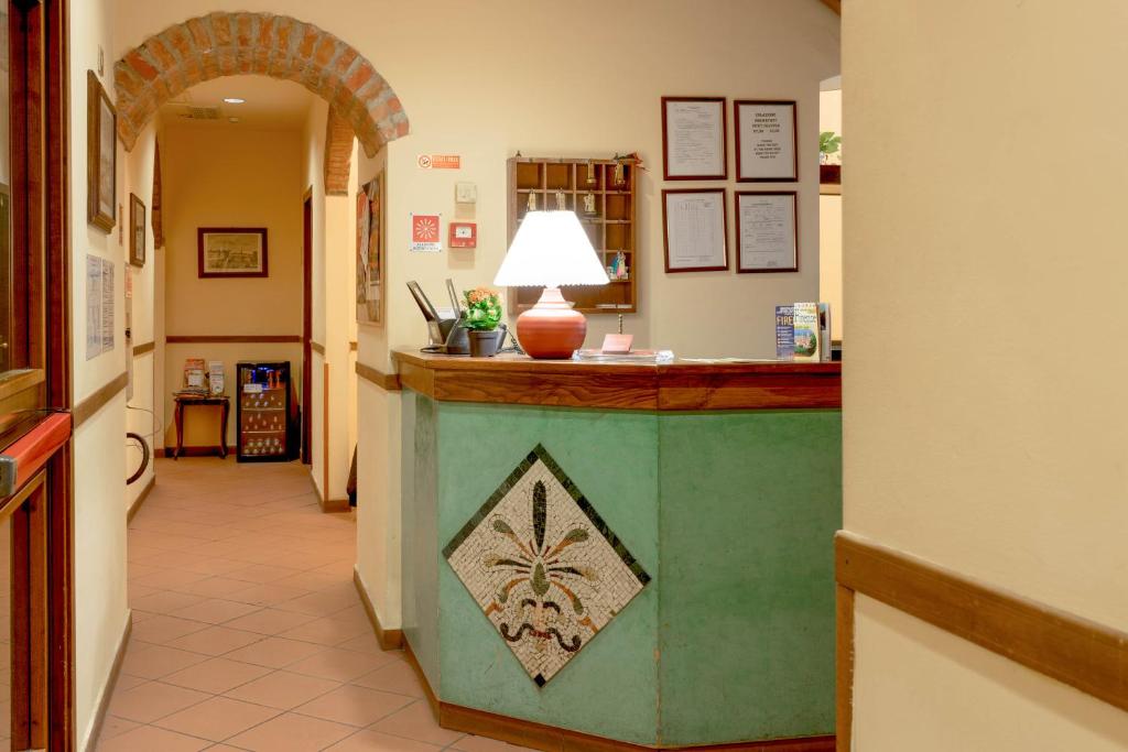 Viesnīcas reģistratūra ar zaļo leti un mozaīkas dizainu, apgaismotu ar lampu. Sienās piekārtas dokumenti un mākslas darbi, redzams apgaismojums un ērta apkalpošana.