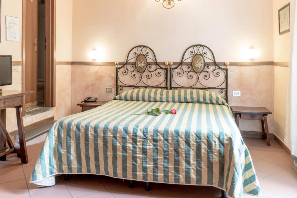 Mājīgā guļamistaba ar metāla gultu un svītrainu gultas veļu, uz gultas novietota roze. Telpa ir gaiša un ērta, ar koka mēbelēm un televizoru.