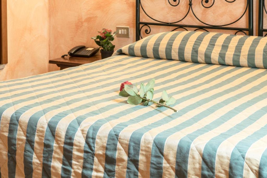 Gultas veļa ar zilu un balto svītru rakstu, uz kuras atrodas rozes zars. Blakus ir neliela ziedu podiņš un telefons uz naktsgaldiņa.