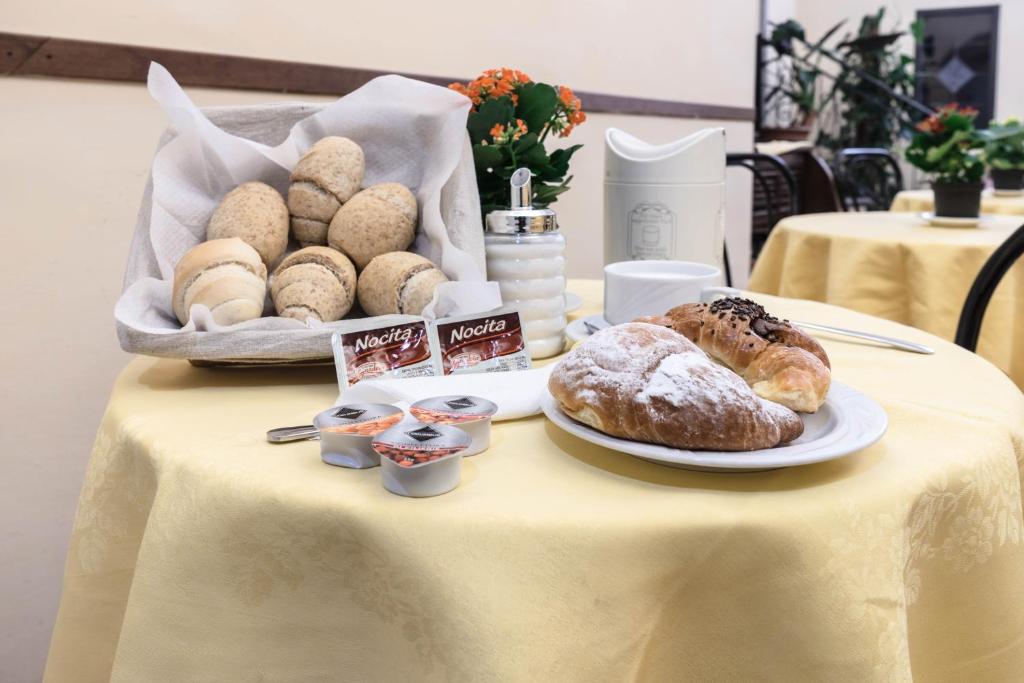 Brosta galds ar šķīvīti, uz kura ir kruasāni un saldējuma mērces, kas pasniegti kopā ar maizes maizītēm un ziediem uz dzeltena galdauta.