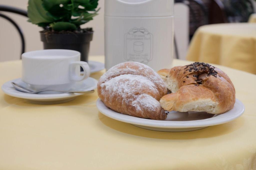 Svaigi cepti kruasāni uz balta šķīvja, blakus balta kafijas tasi un karote, viss uz dzeltena galda.