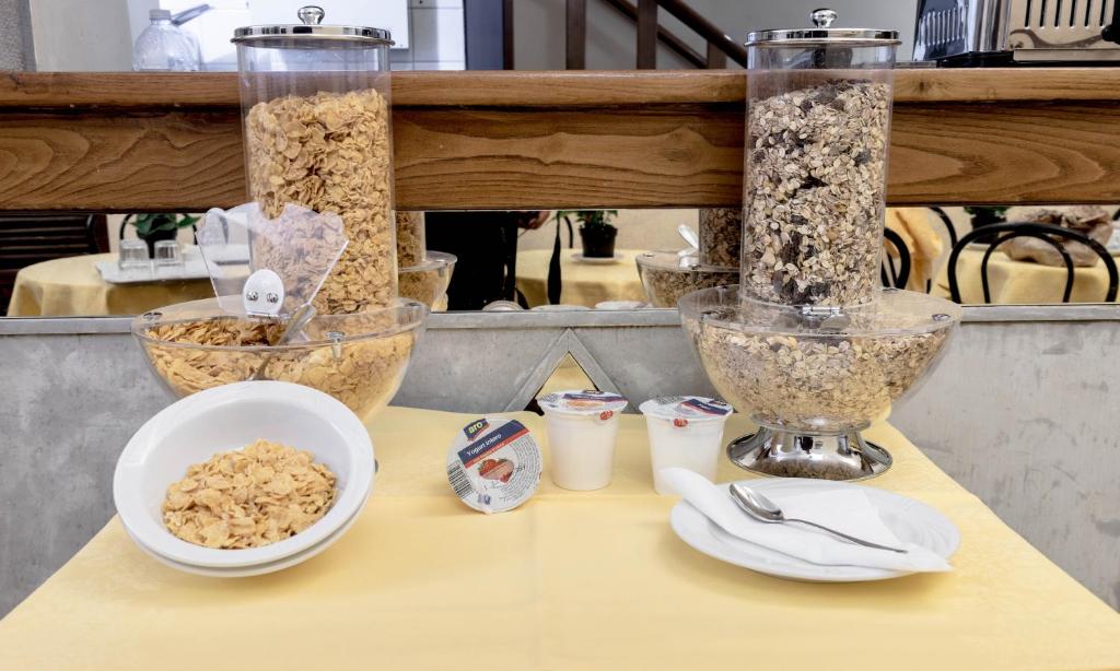 Brokastīs piedāvātie graudaugi un jogurts, kas sakārtoti uz galda ar dzeltenu galdautu. Redzami dažādi graudu veidi un servēšanas trauki.