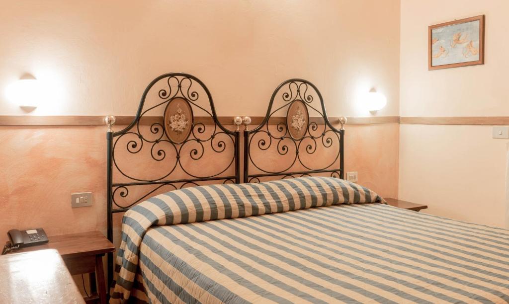 Guļamistaba ar metāla gultas rāmi un svītrainu gultas veļu, gaiši rozā sienām un siltu apgaismojumu. Telpā redzama arī telefons un neliels galds.