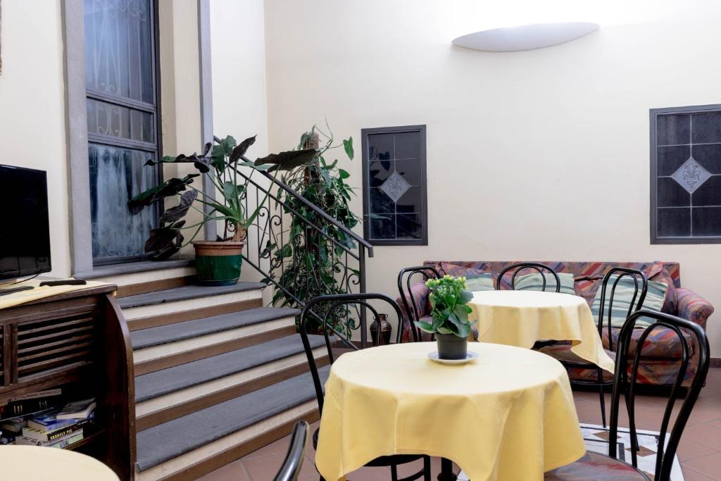 Mierīgas iekštelpas ar dzeltenām galdautām, zaļām augiem un soļiem, kas ved uz augšējo stāvu. Sēdvietas un televizors pie sienas rada mājīgu atmosfēru.